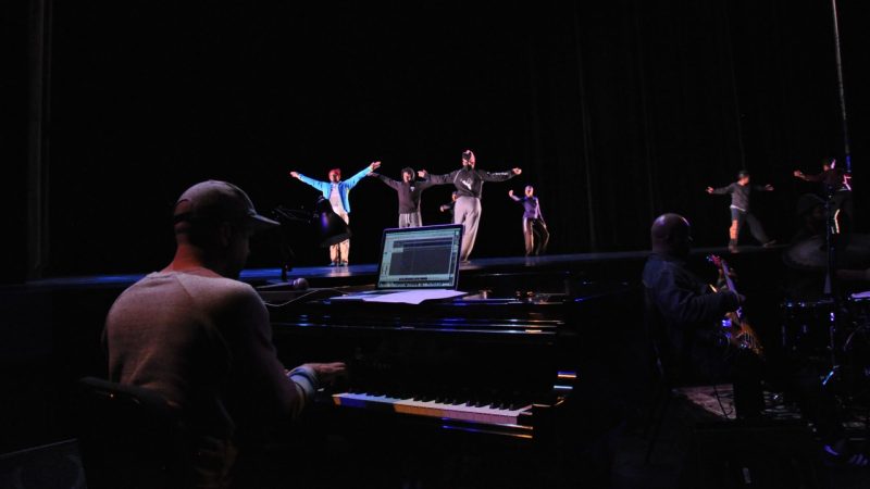  Dark image inside the Fife theatre. Jason Moran playing piano with performers dancing on stage behind him