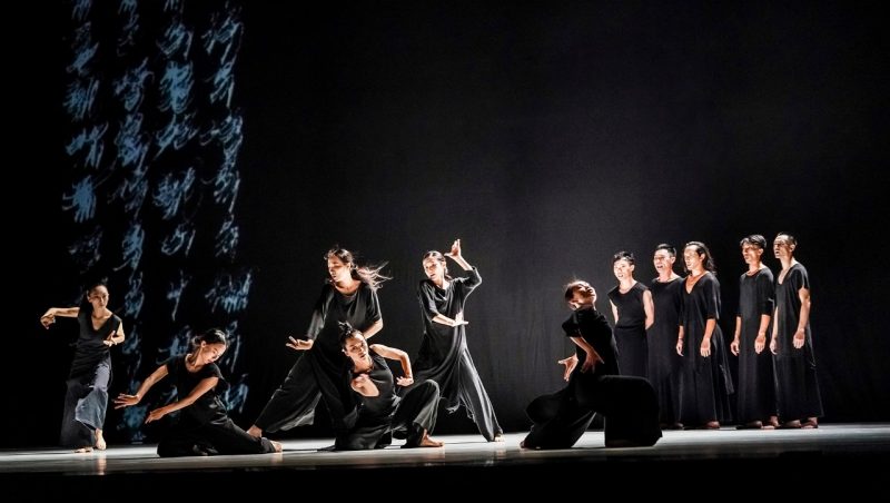 The dancers of Cloud Gate Dance Theatre of Taiwan wear all black and perform on stage, a projection of four towering columns of Chinese characters behind them. Photo by LIU Chen-hsiang
